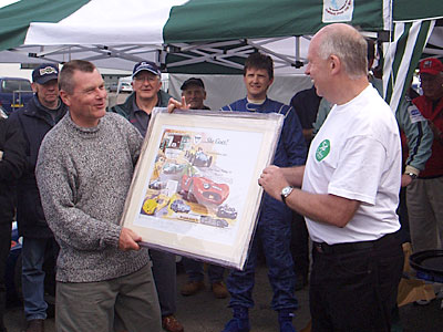 Roger Dunbar, wearing the special Mallory t-shirt while presenting F/J race winner Martin Walford with his prize, one of the multi-signed ELVA Prints.
